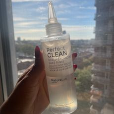 a hand holding a bottle of haircare product in front of a window