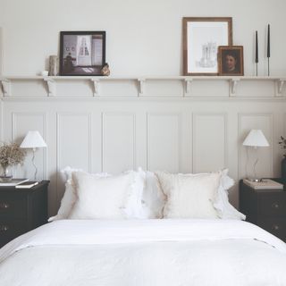 A bedroom with a symmetrical set-up, white bedding, cream wall panelling and matching wiggly table lamps