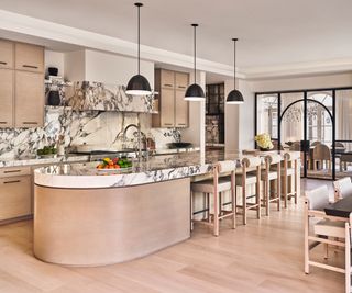 kitchen with marble countertop and backsplash and pale wood curved island with dining room through arched windows