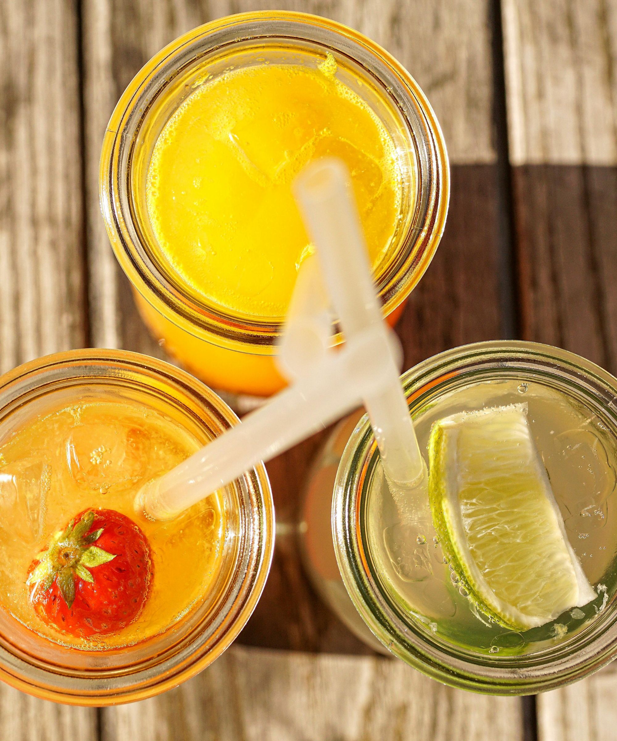 Aerial view of orange and lime cocktails served in mason jars with clear plastic straws, sitting on a wooden table