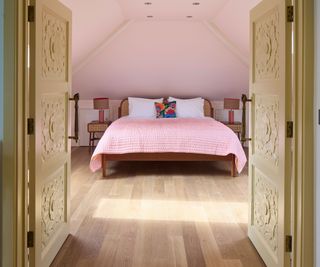 bedroom with pale engineered wood flooring with carved double doors and pink bedspread 