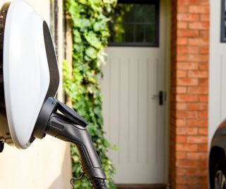 An electric car charging point mounted to a wall at a home with a black plug in it. A front door out of focus in the background