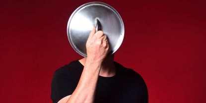 A man holds a cooking pot lid in front of his face.