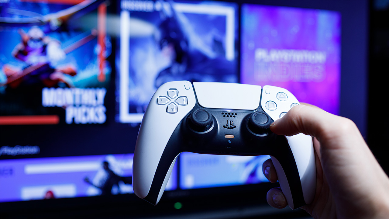 Person holding white PS5 controller, with blurred screen in the background displaying "monthly picks" games