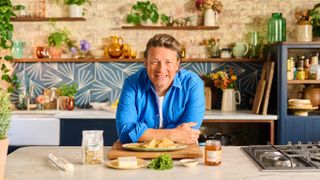 Jamie Oliver in a blue shirt leaning against a kitchen counter for Jamie's 5 Ingredient Meals