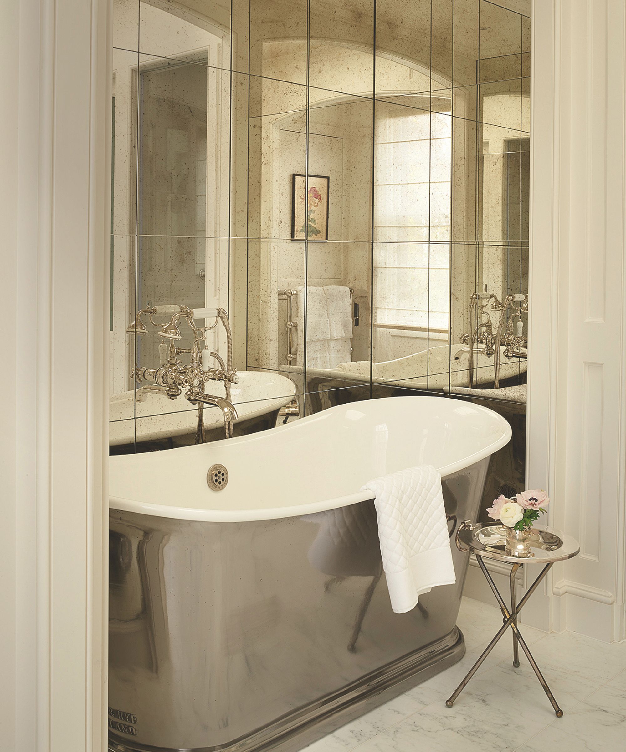 Elegant bathroom with a free-standing, silver-finished tub set against walls covered in antique-style mirrored tiles
