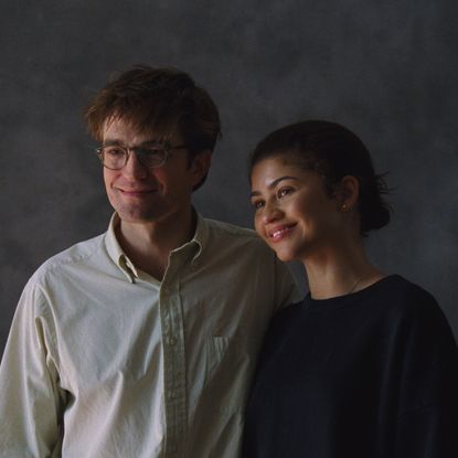 robert pattinson and zendaya as charlie and emma trying to smile and pose for wedding photos in a photo studio in a still from the movie the drama