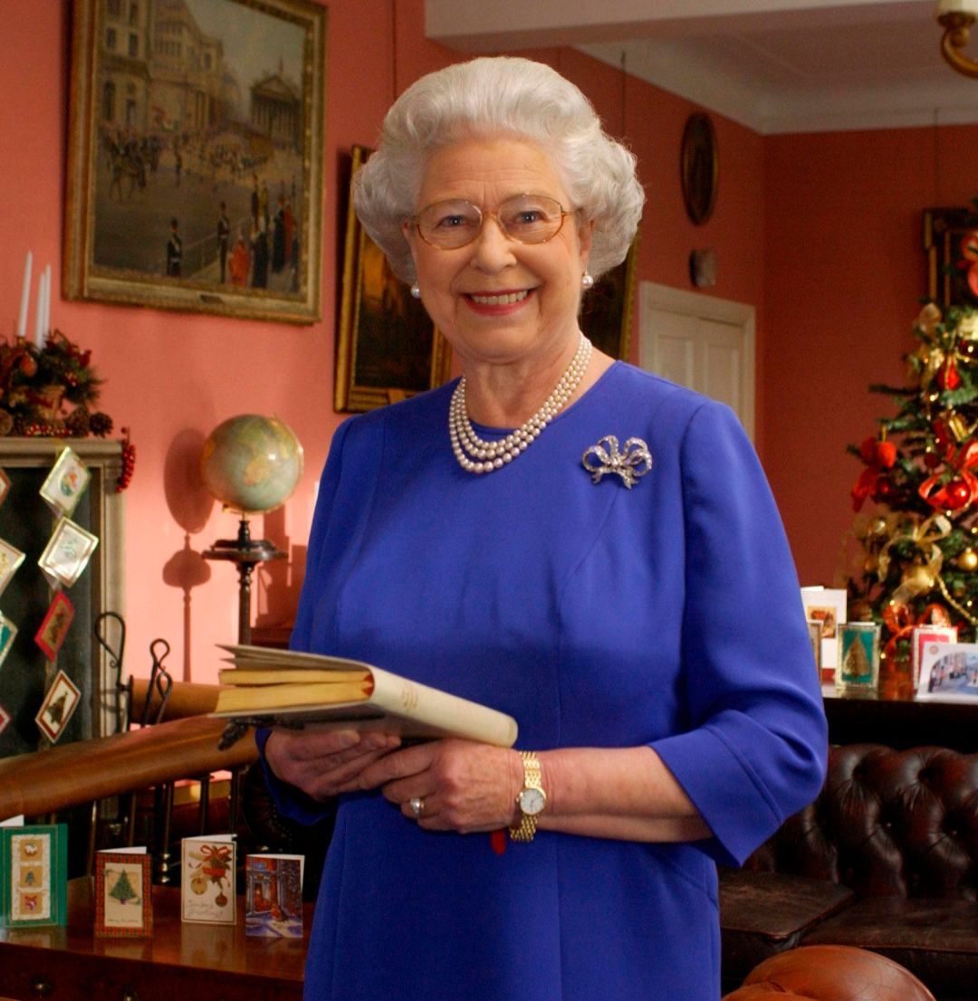 Queen Elizabeth wearing a blue dress standing in front of a Christmas tree
