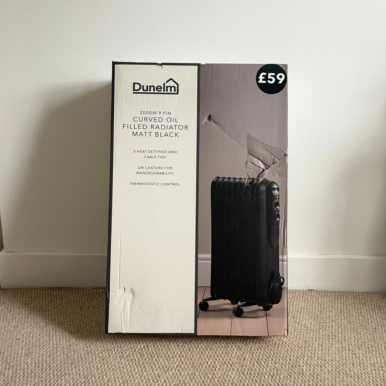 The box of the 2000W Contemporary Round 9 Fin Oil Filled Radiator leaning up against a white wall