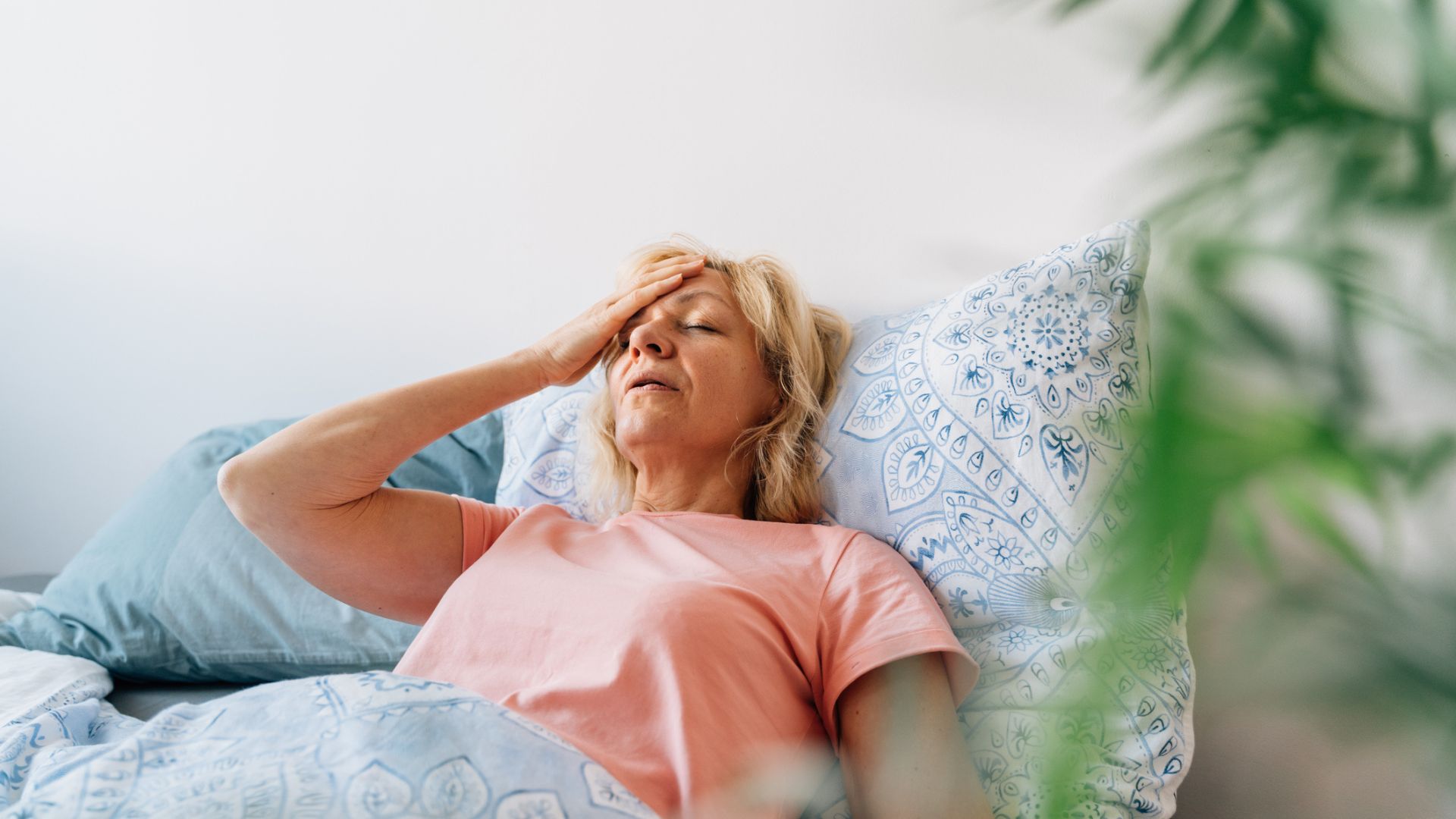 An older woman lying in bed sweating with her hand on her forehead