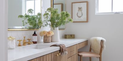 bathroom vanity with bar stool, vase of flowers, soap, gold hardware, and art on wall