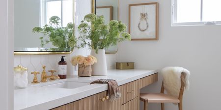 bathroom vanity with bar stool, vase of flowers, soap, gold hardware, and art on wall