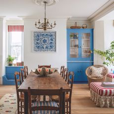 open plan kitchen dining area with farmhouse table, blue painted dresser and red and white striped ottoman