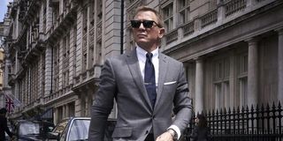 James Bond (Daniel Craig) walks suavely in a grey suit and designer sunglasses in No Time To Die.