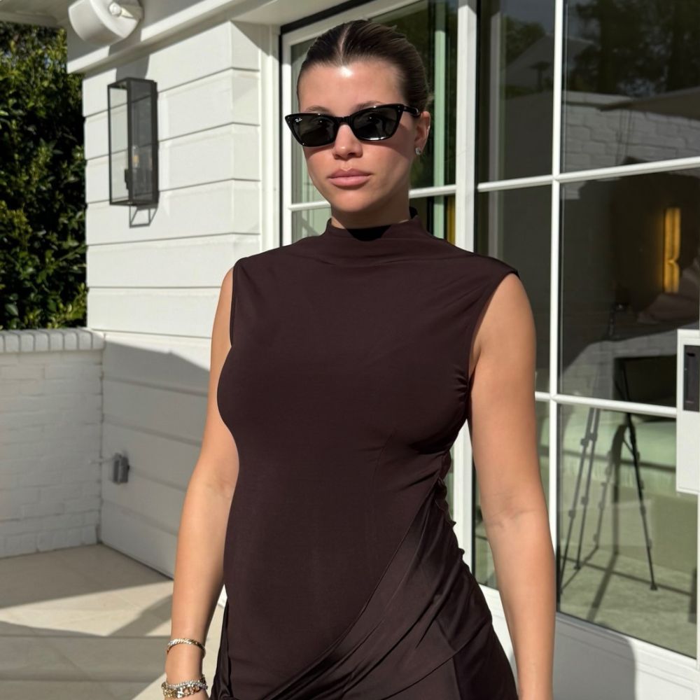 Sofia Richie Grainge wears a chocolate brown dress with a burgundy clutch bag and dark sunglasses.