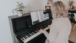 Woman plays her digital piano with a tablet and music book in front of her