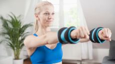 woman wearing blue crop top extending her arms out straight in front wearing wrist weights 