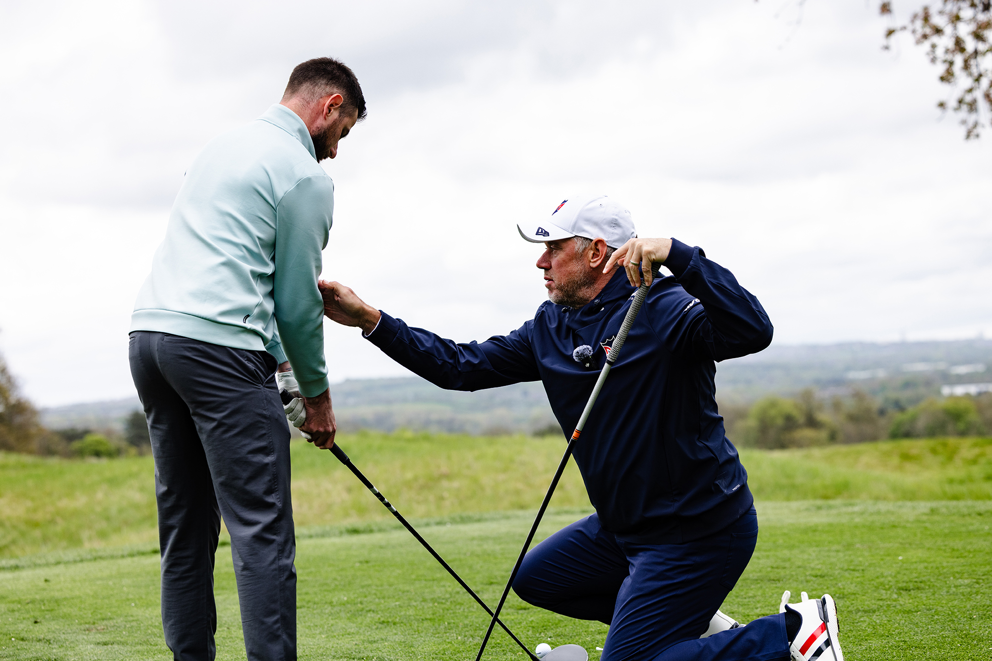 Lee Westwood manoeuvring Baz Plummer into the correct set up position with driver during a golf lesson