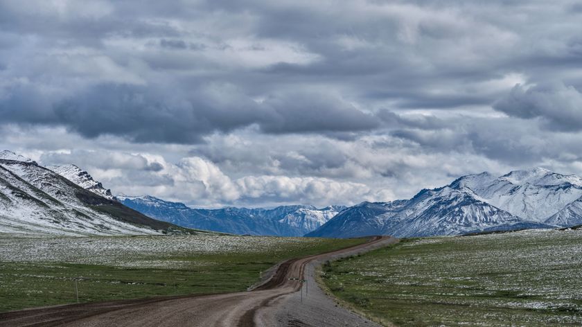 long road along tundra with mountains in background and cloudy sky