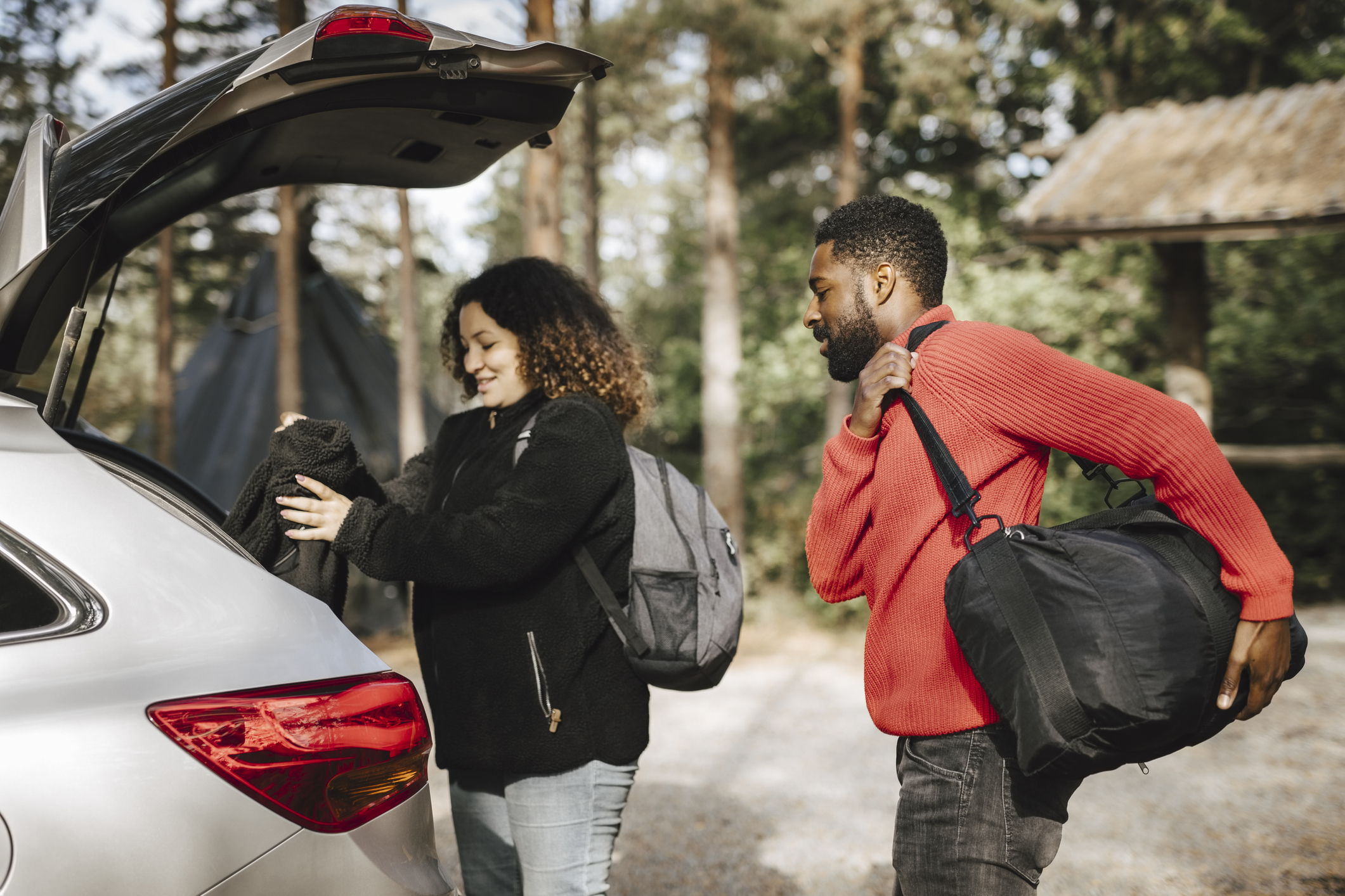 A couple puts luggage in the trunk of a car.
