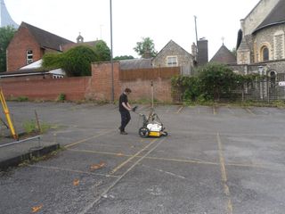 A researcher conducts a ground-penetrating radar (GPR) survey of a parking lot in Reading, England, beneath which are part of the grounds of medieval Reading Abbey. The survey uses radar waves to detect structures and anomalies under the surface, which could include building foundations or even the grave of Henry I, the English king buried near the abbey's high alter.