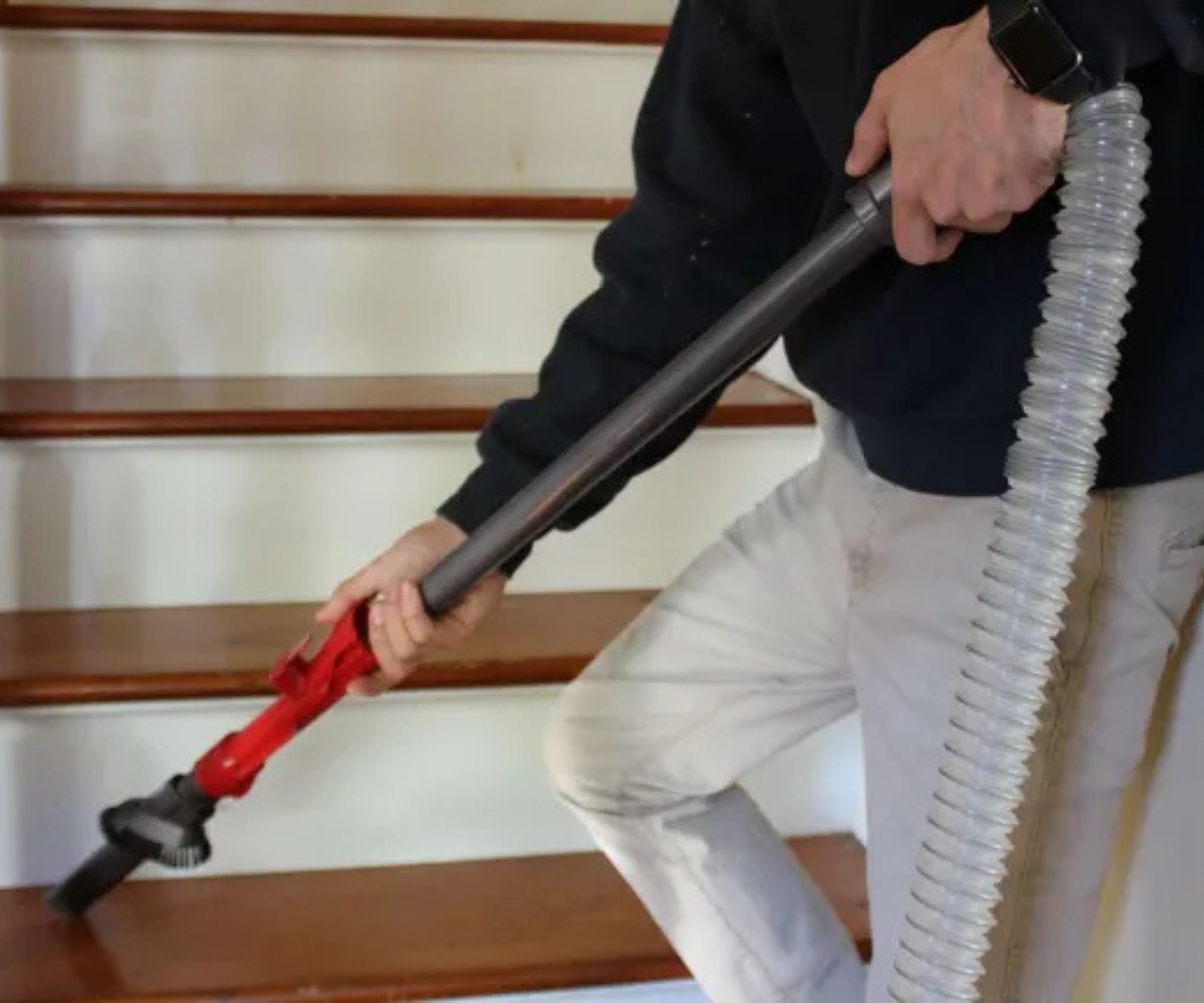 Person wearing white jeans and black top, vacuuming stairs using a hose, wand and cleaning attachment of the Dyson Ball Animal 3 in Camryn Rabideau's home.