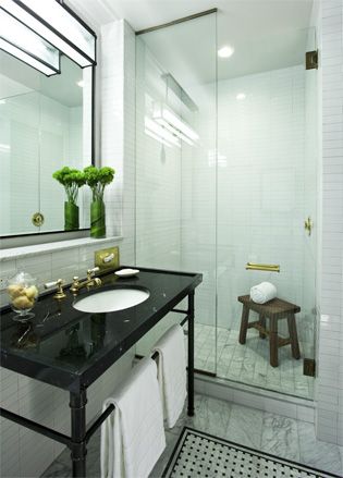 Refinery Hotel, New York, USA. A bathroom with a black vanity, a large wall mirror an a shower with a wooden stool inside of it.