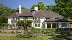 an exterior shot of a large English home in Surrey with a tiered garden surrounded by trees