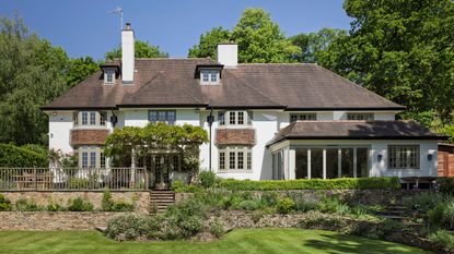 an exterior shot of a large English home in Surrey with a tiered garden surrounded by trees