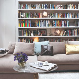 A living room with a built-in library and a chaise grey sofa with paper lantern lamps on the shelves