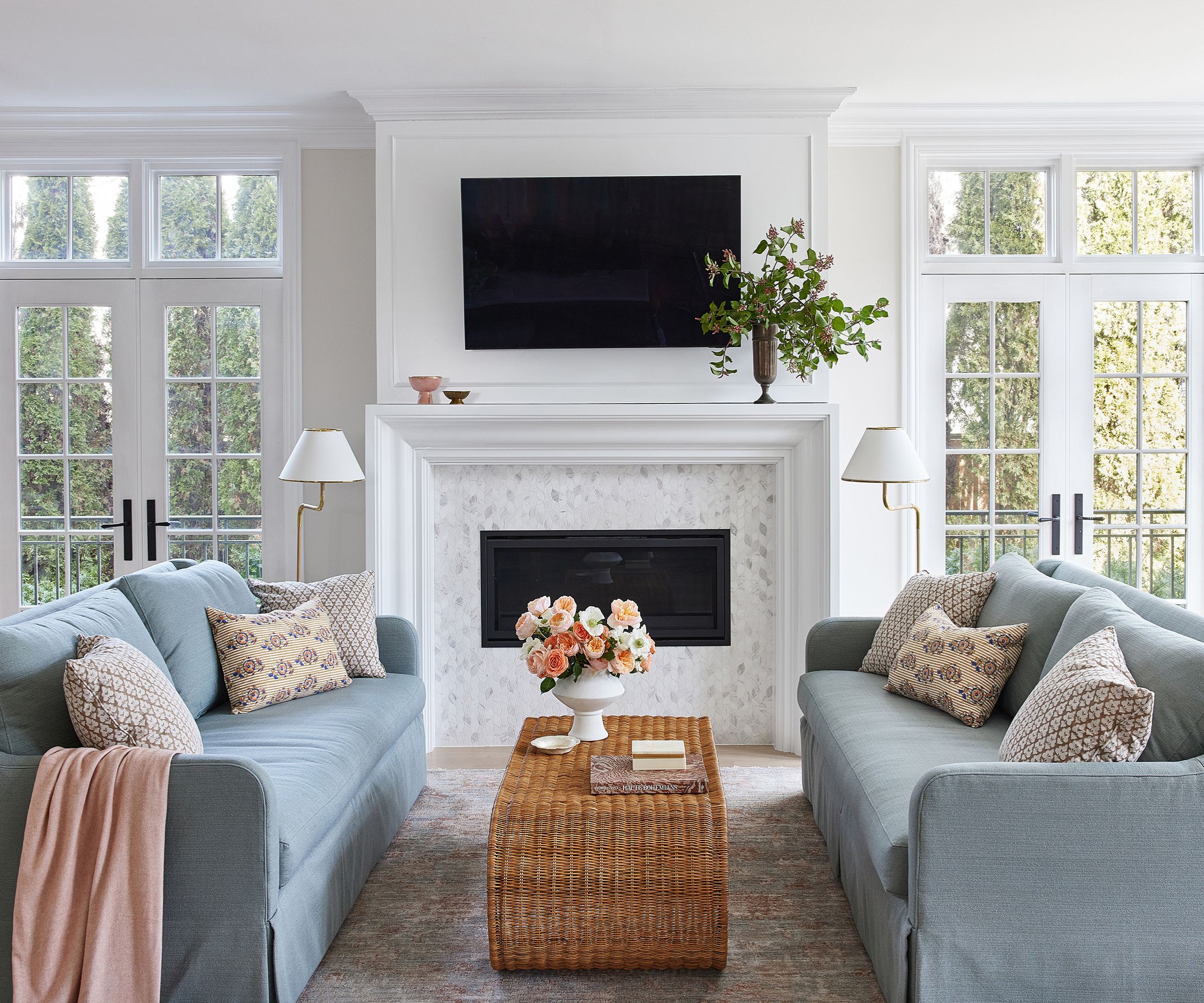 Living room with pale grey walls, white trim, French doors, blue sofas, rattan coffee table and floral cushions