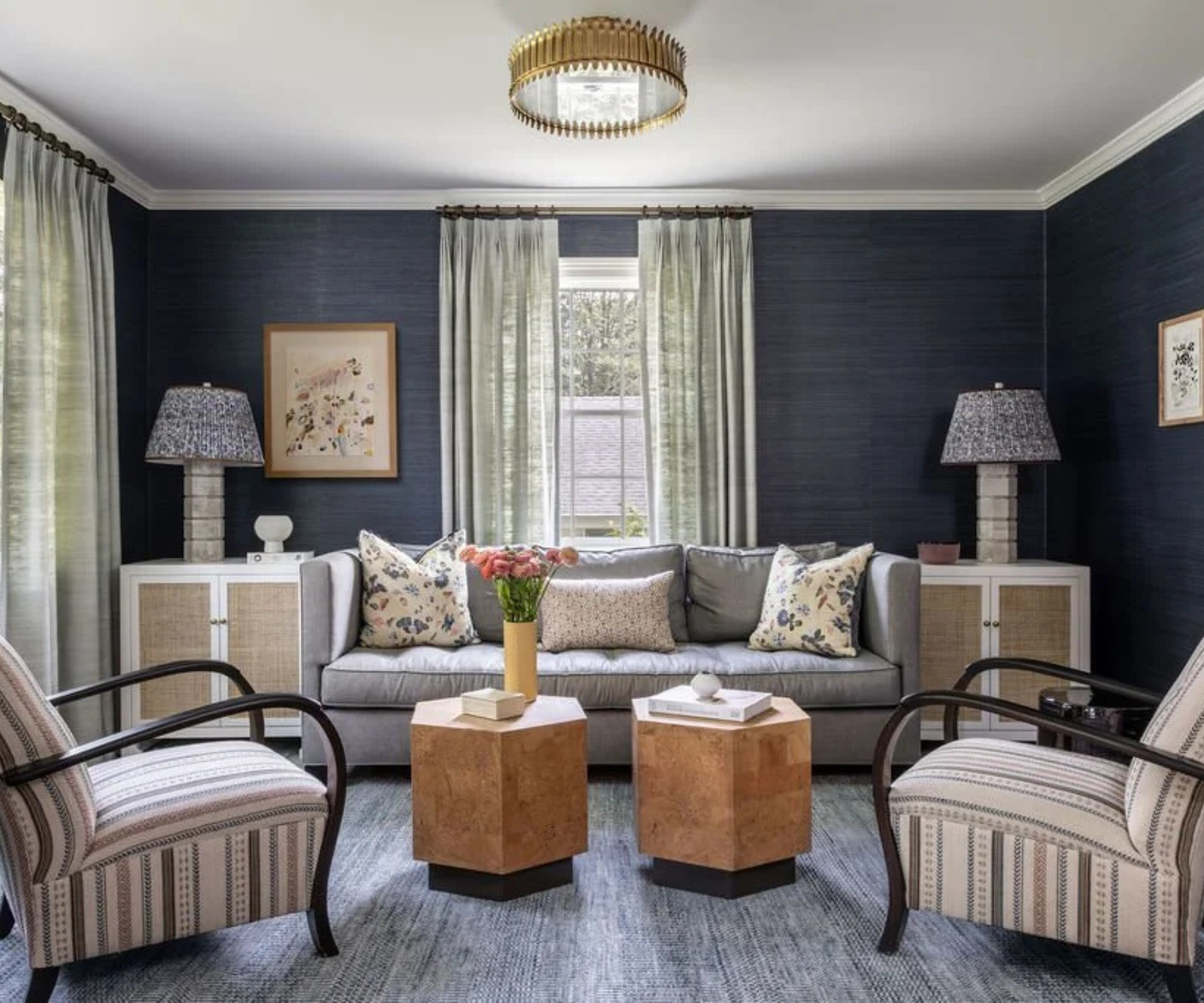 a sitting room with blue grasscloth walls, a blue couch, matching side tables on either side with lamps on top, two tables in the center of the room, and two chairs on either side