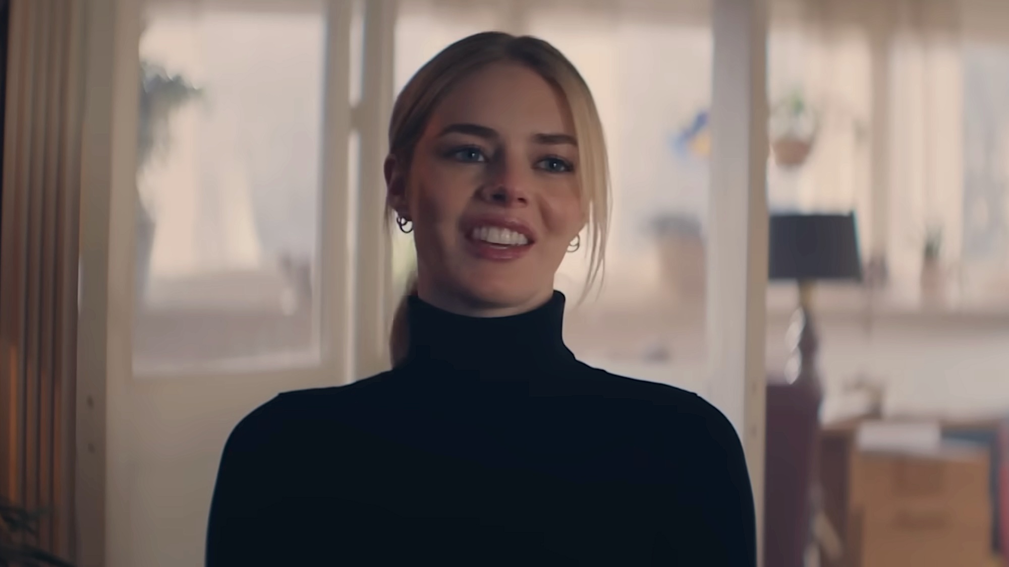 Lisa in black turtleneck sweater smiling sarcastically at Dan in Over Your Dead Body