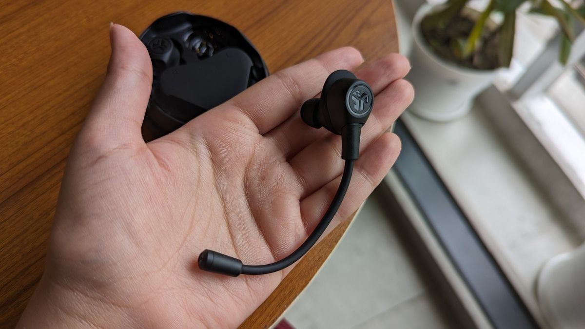 JLab Work Buds wireless earbud with detachable microphone held in hand with the case kept on a table in the background.