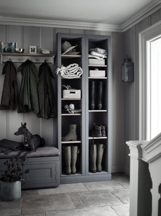 grey toned boot room from neptune, with open shelving full of boots and towels, and a bench with a black dog on it, and gray tiled floor