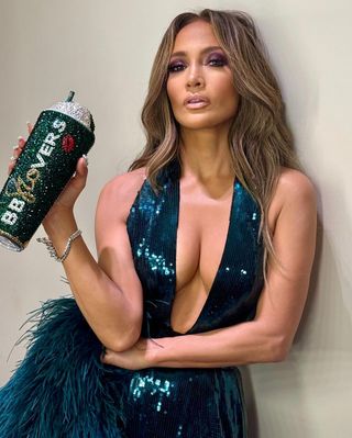 jennifer lopez wears a teal sequin gown with feathers and a matching rhinestone tumbler