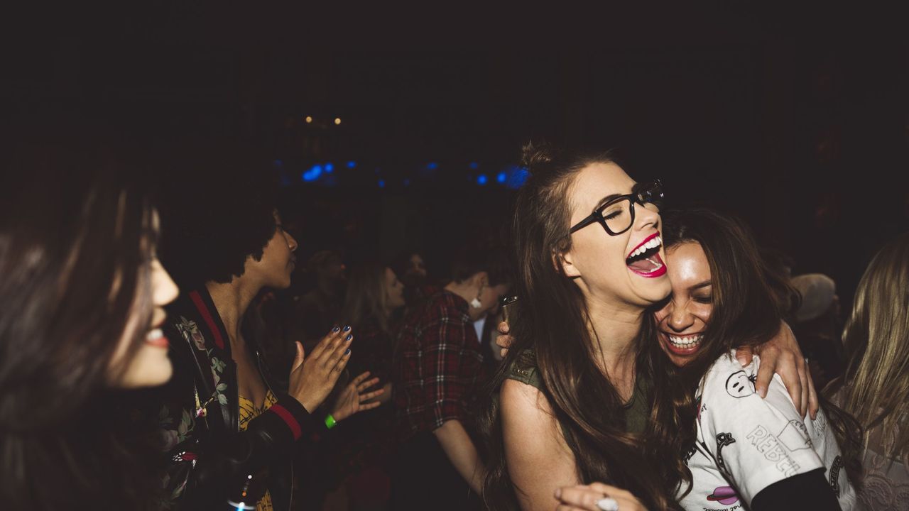 Laughing, happy, carefree young female milennials dancing, partying at nightclub