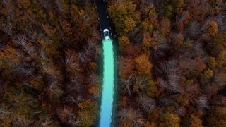Directly above picture made by drone of an electric car driving through autumn forest, leaving behind a bright trace made by the sustainable energy, an the zero emissions.