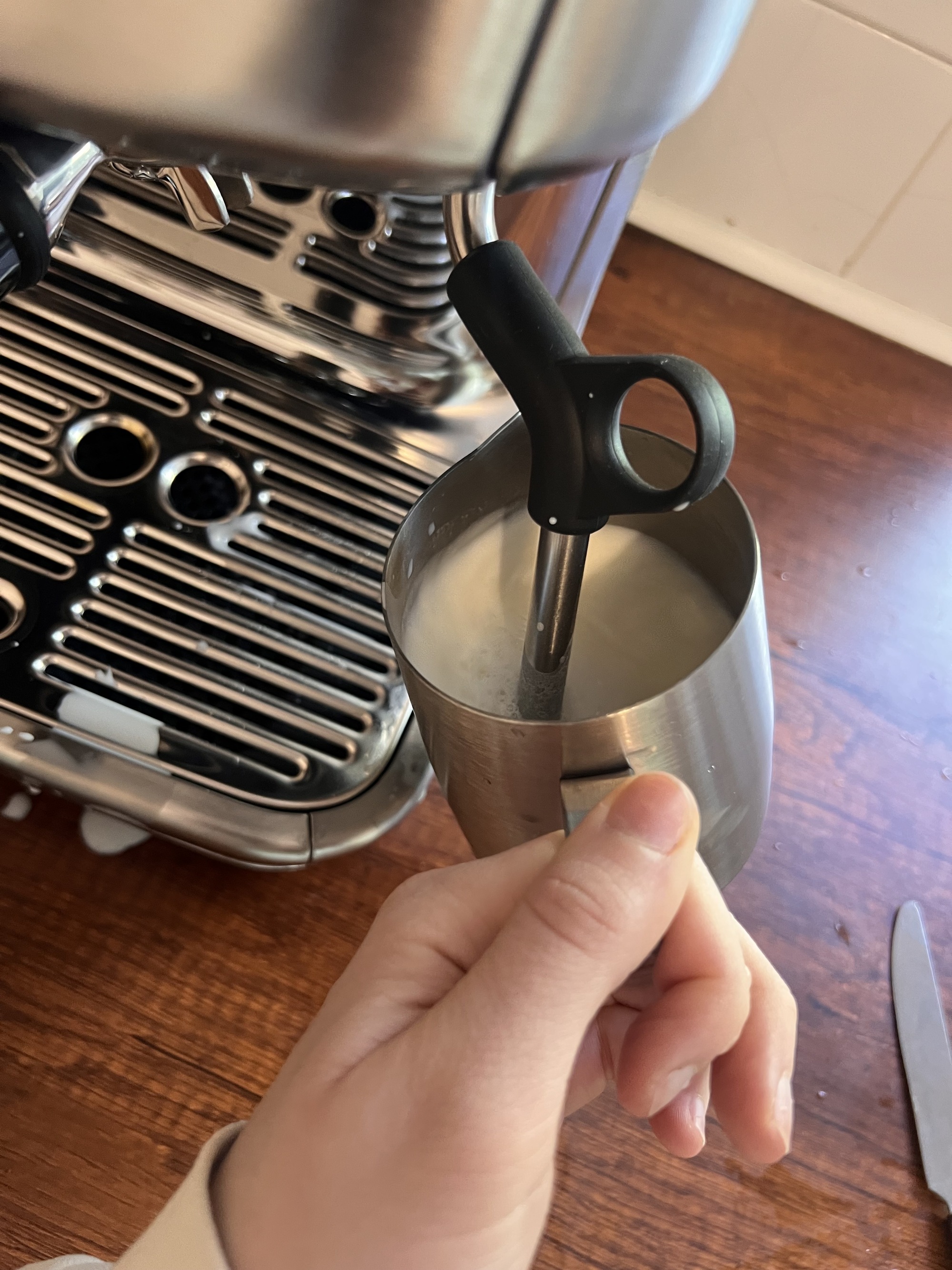A hand frothing milk in a silver coffee machine