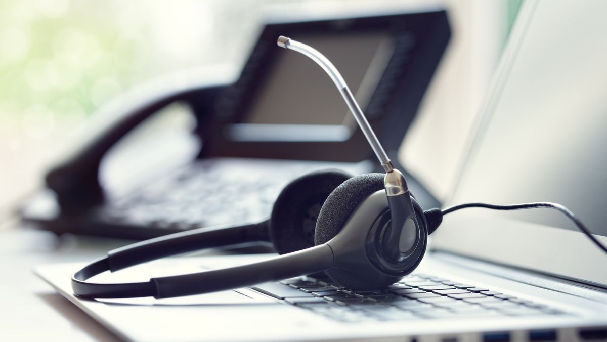 A headset lying on a keyboard with a blurry phone in the background