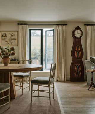 neutral dining room with a large round wooden table and a large ornate mahogany grandfather clock