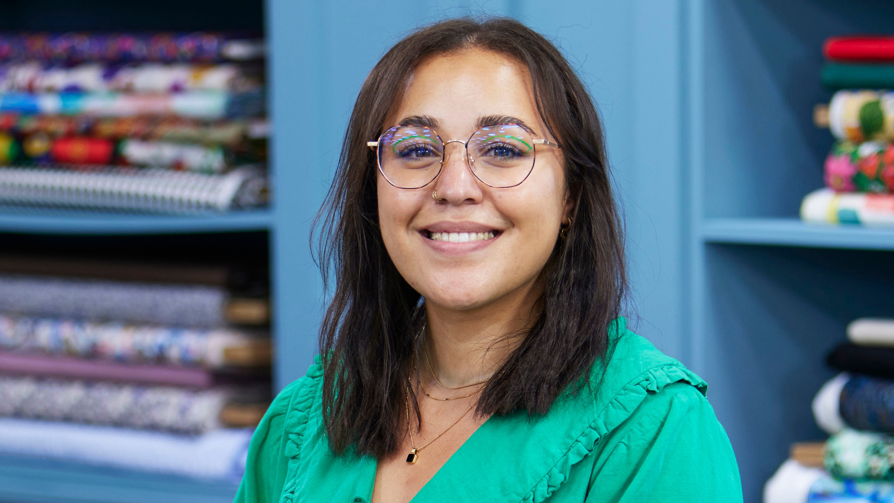 Yasmin standing in the Great British Sewing Bee studio and smiling for the camera