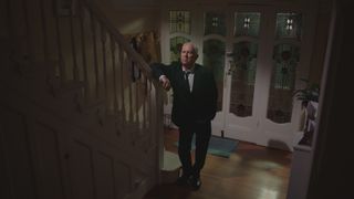 Charlie in a funeral suit standing alone at the bottom of the stairs in the home he shared with Duffy
