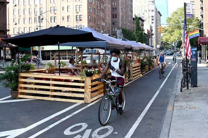 A person on a bicycle wearing a face mask rides past outdoor seating as the city continues Phase 4 of re-opening following restrictions imposed to slow the spread of coronavirus on August 11,