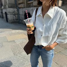 A woman wearing skinny jeans, a tote bag, and a white button-down shirt.