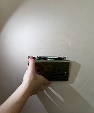 Hand pulling outlet socket away from the wall and looking for stud