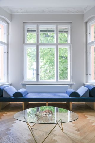 A long daybed in blue, and a glass coffee table placed in front