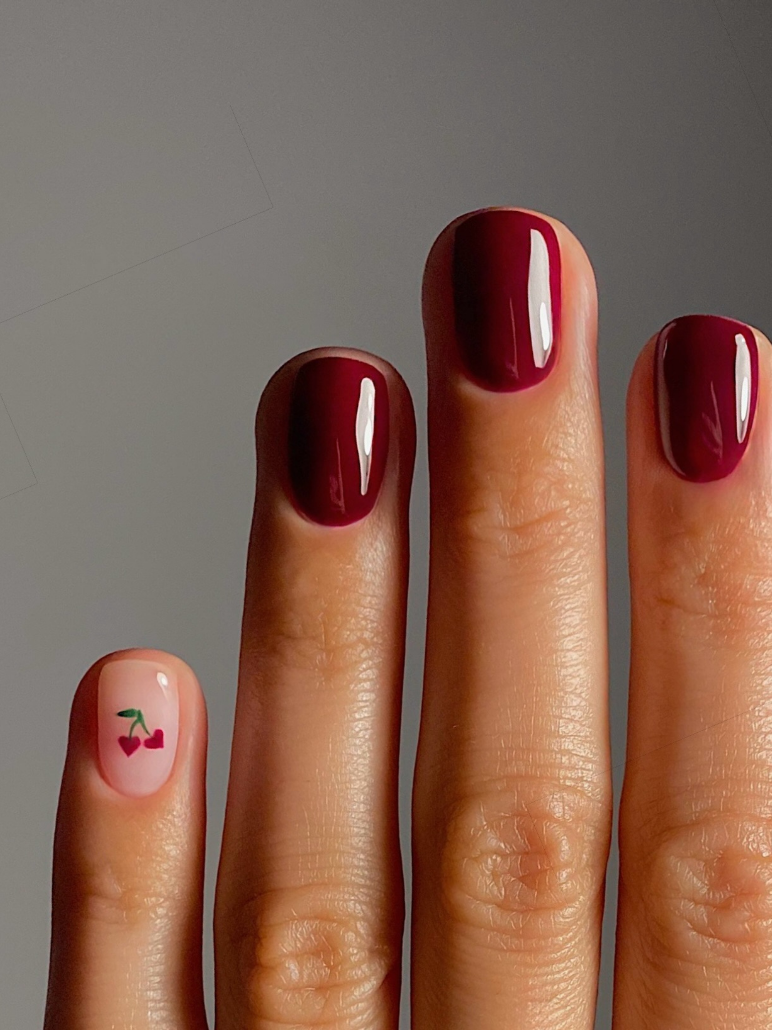 Short nails painted in a dark cherry shade, one nail has a tint cherry icon detail