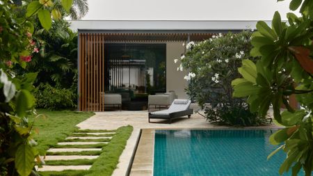 A garden with a pool, a sun lounger, and flowering trees
