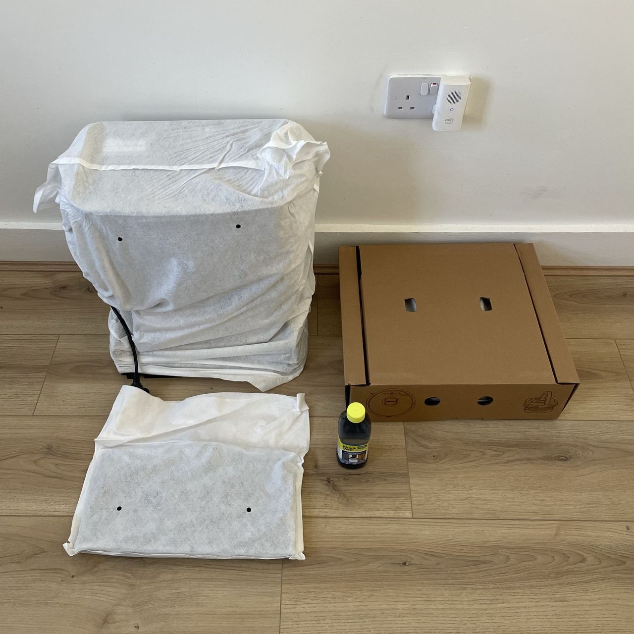 Components of the Shark PowerDetect UV Reveal 2-in-1 Vac &amp; Mop Robot Vacuum sitting on the floor, wrapped in packaging